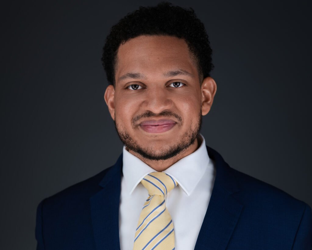 Professional headshot of Dominic Naimool wearing business attire and smiling at the camera.